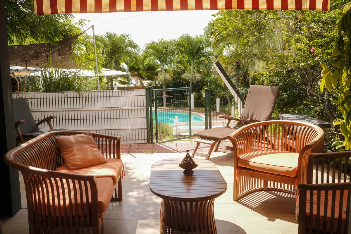 Terrasse couverte avec fauteuils en teck, store rayé et vue sur la piscine